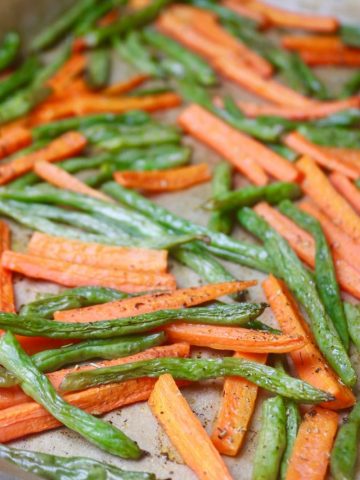 Roasted carrots and green beans on a parchment lined baking sheet