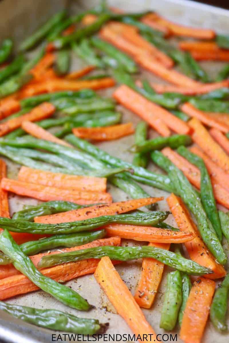 Roasted carrots and green beans on a parchment lined baking sheet