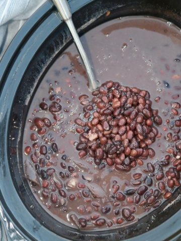 ladle scooping black beans from a slow cooker