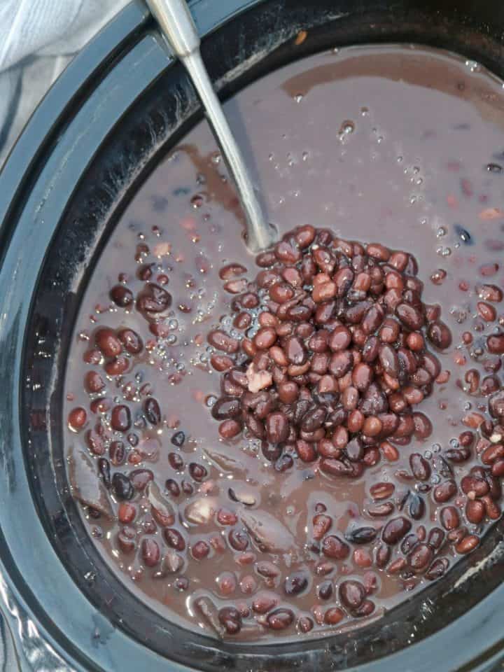 ladle scooping black beans from a slow cooker