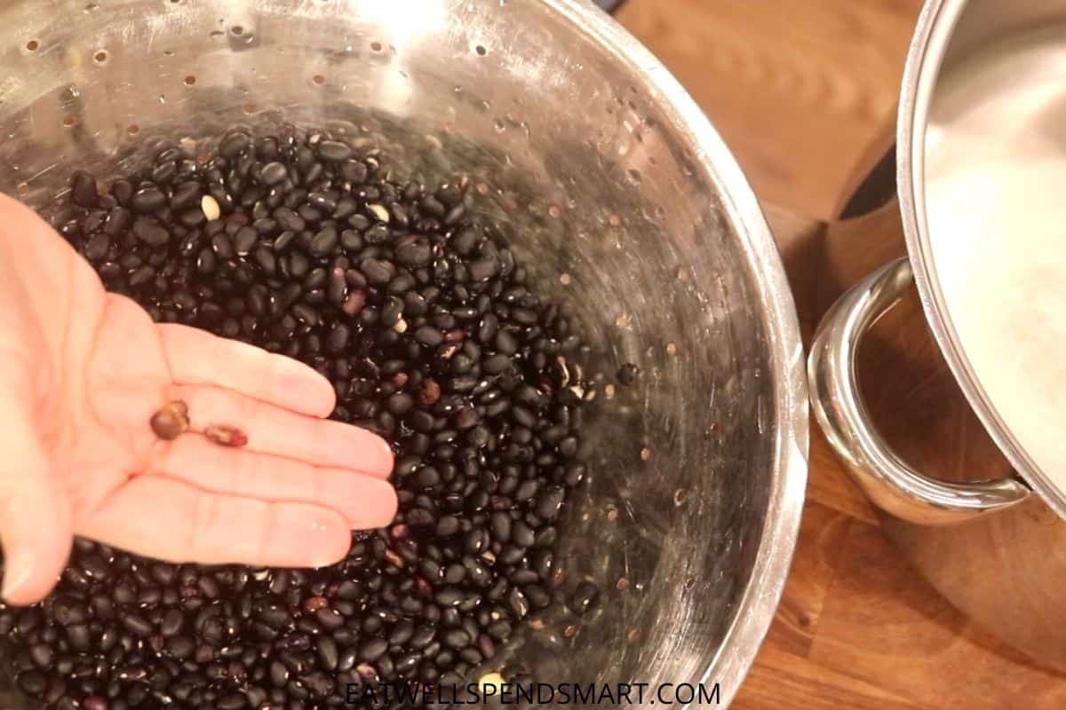 hand picking out bad black beans from a colander