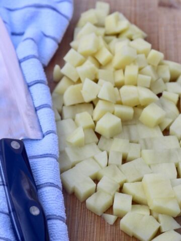cubed potatoes on a cutting board next to a knife and white striped towel