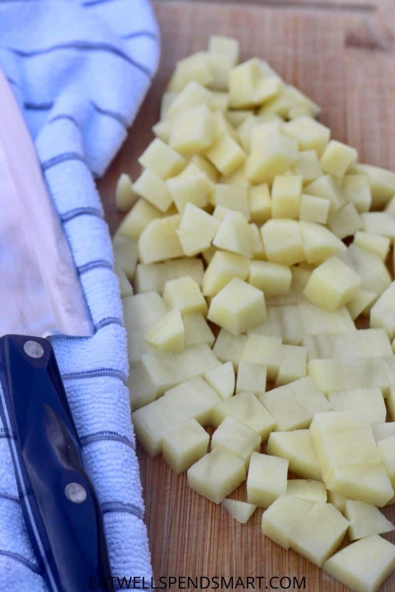 cubed potatoes on a cutting board next to a knife and white striped towel