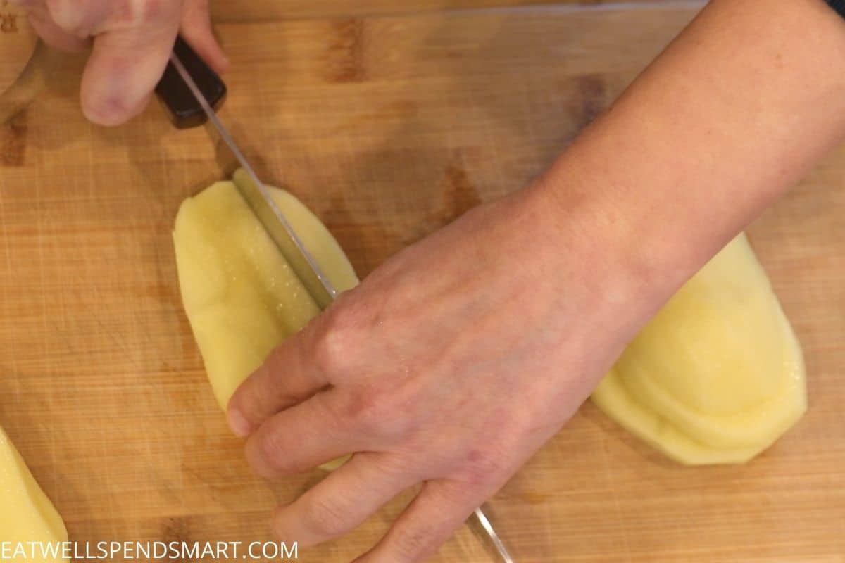 knife cutting sliced potato while hand braces the potato