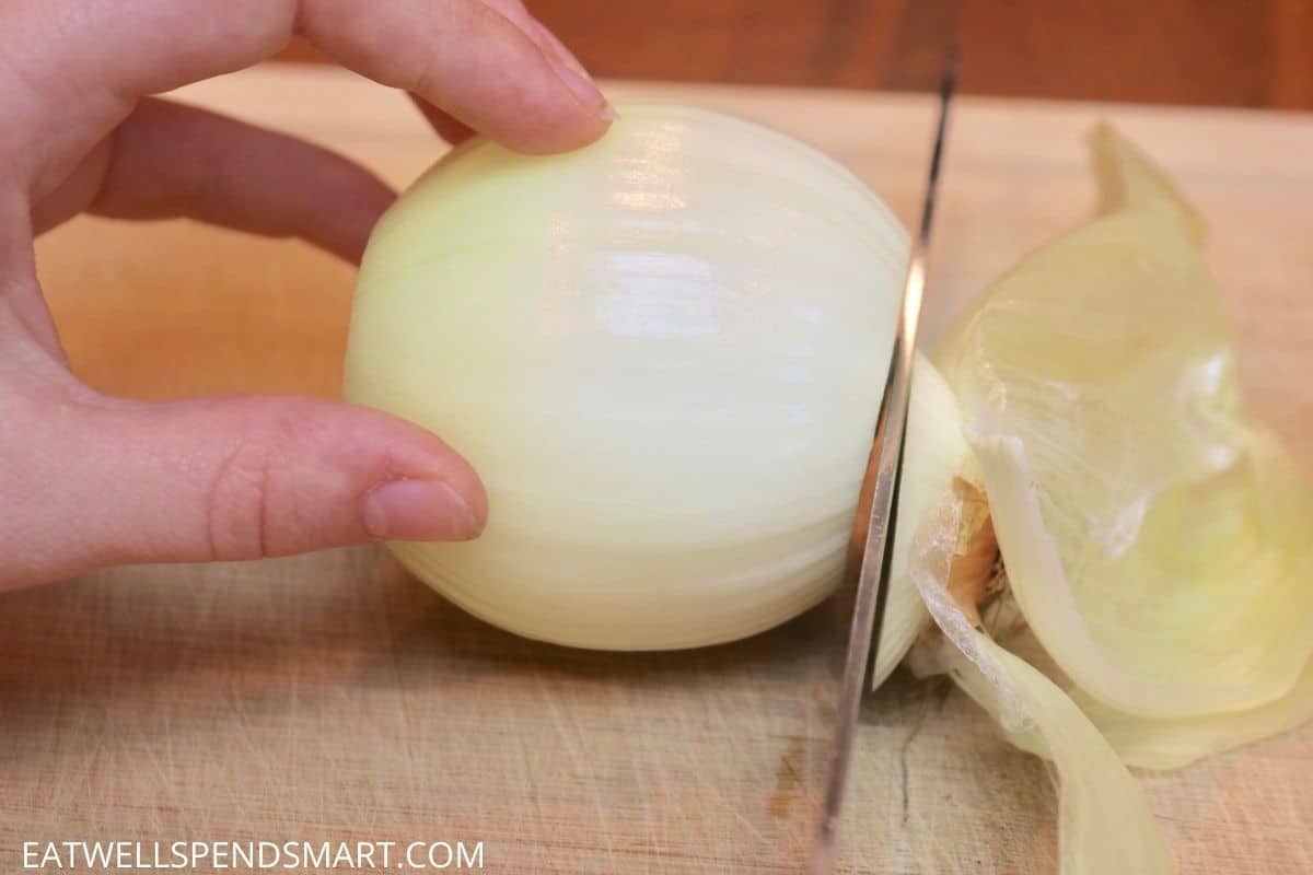 knife cutting root end off onion