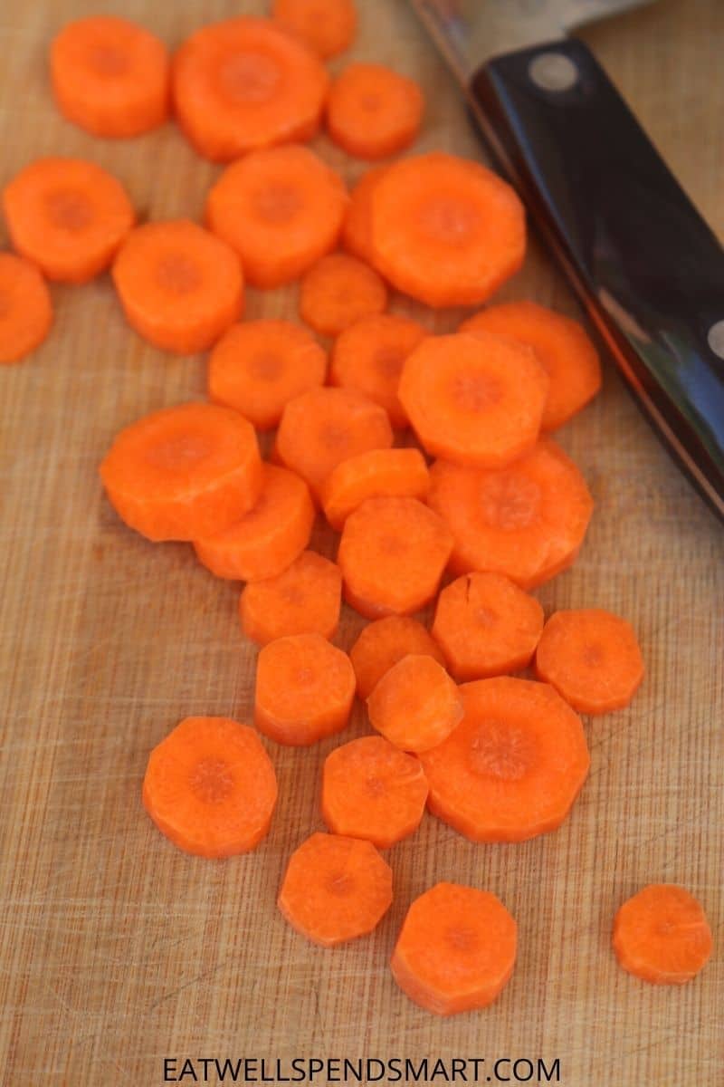 sliced carrots and a chef knife on a wooden cutting board