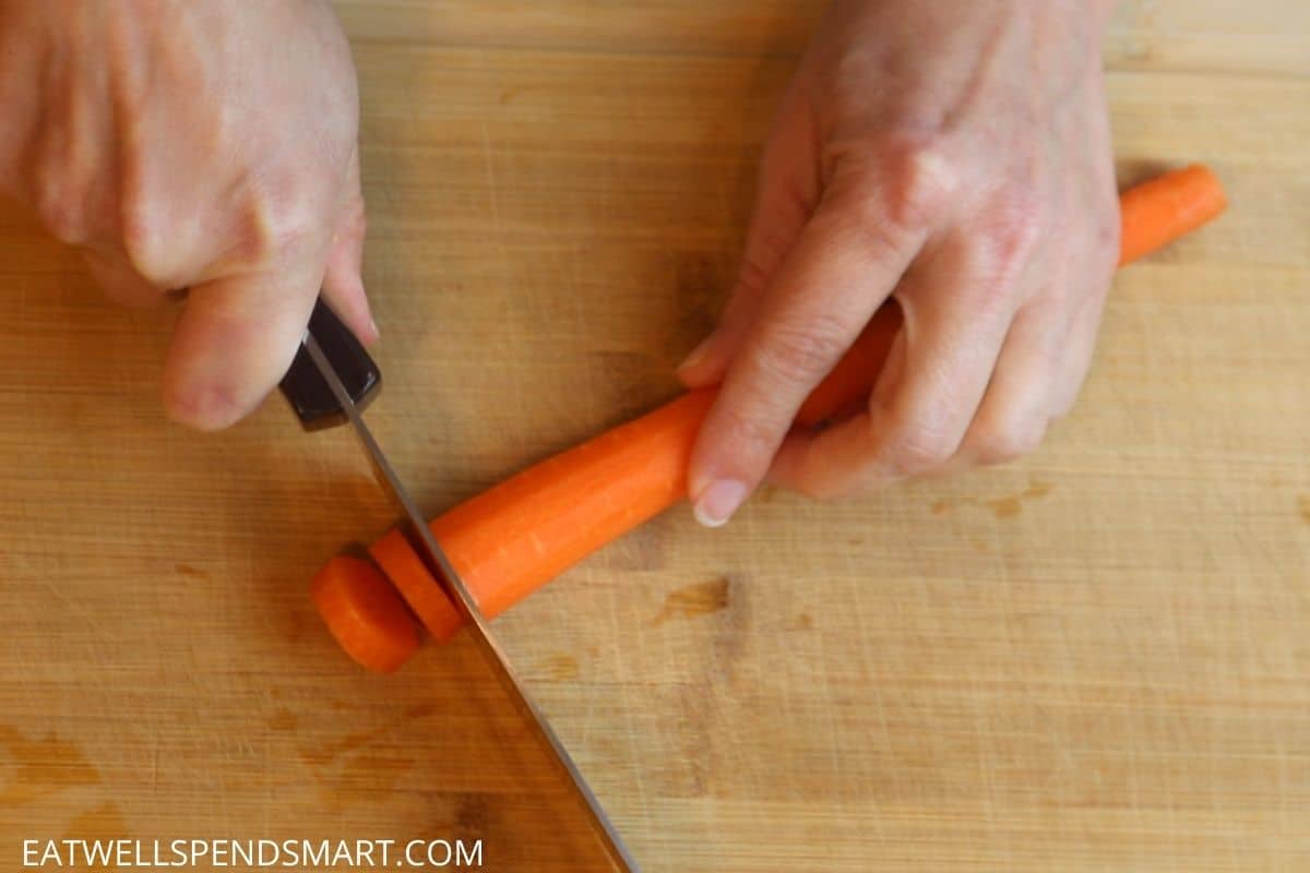 chef knife slicing carrot rounds on a wooden cutting board