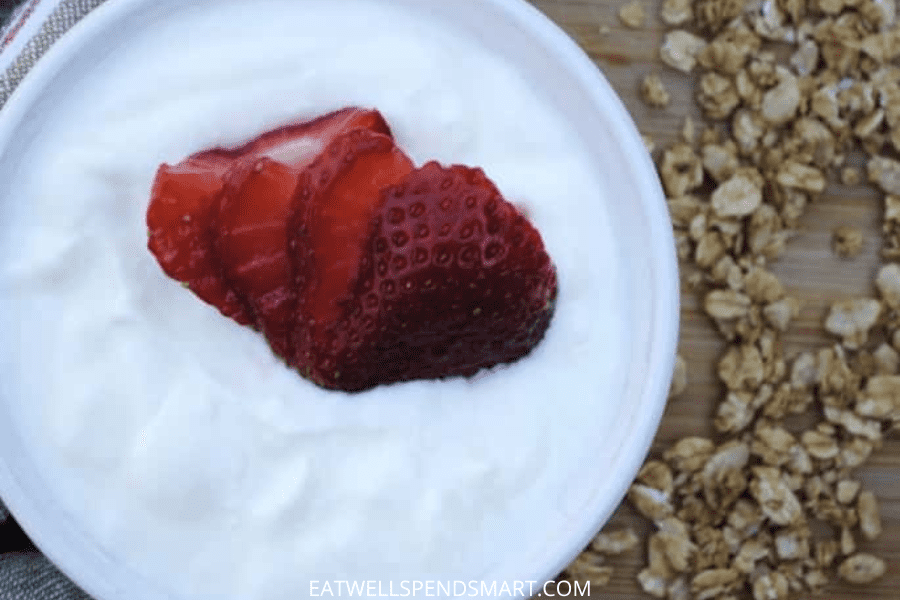 plain yogurt top with strawberries in a white ramekin with oats scattered on the side