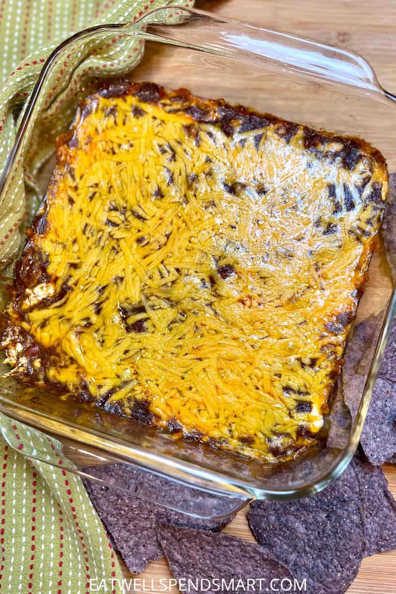 chili cream cheese dip in a square glass dish surrounded by a green towel and blue corn tortilla chips