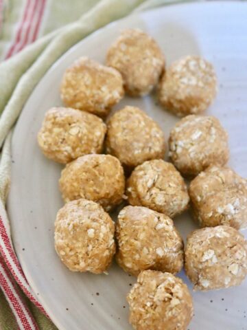 13 peanut butter oatmeal balls on a white plate surrounded by a green and red striped towel