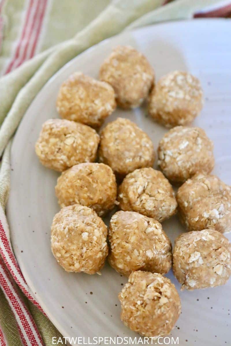 13 peanut butter oatmeal balls on a white plate surrounded by a green and red striped towel