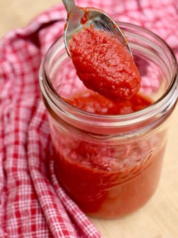 homemade pizza sauce dripping from spoon into jar of more sauce