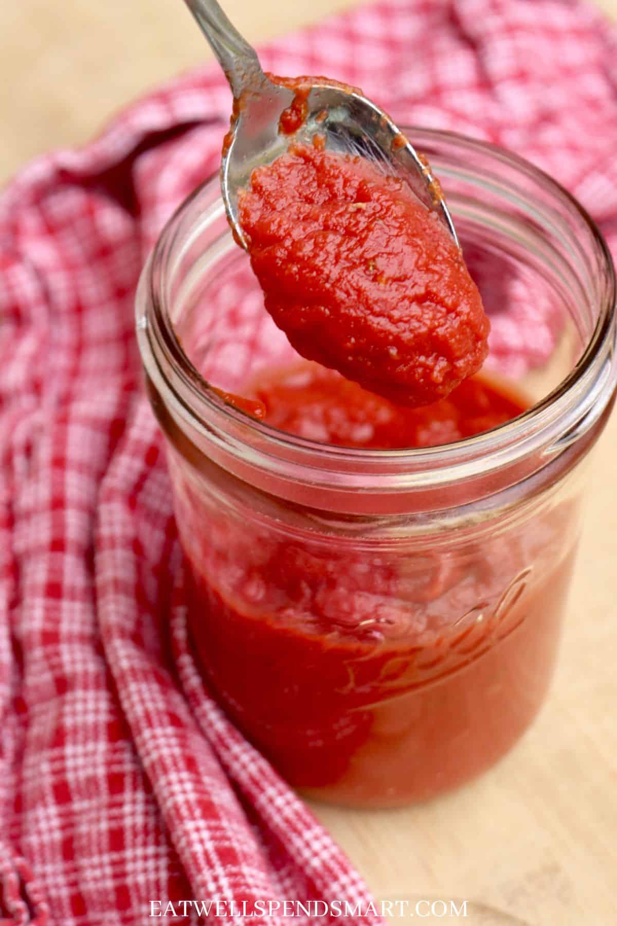 homemade pizza sauce dripping from spoon into jar of more sauce