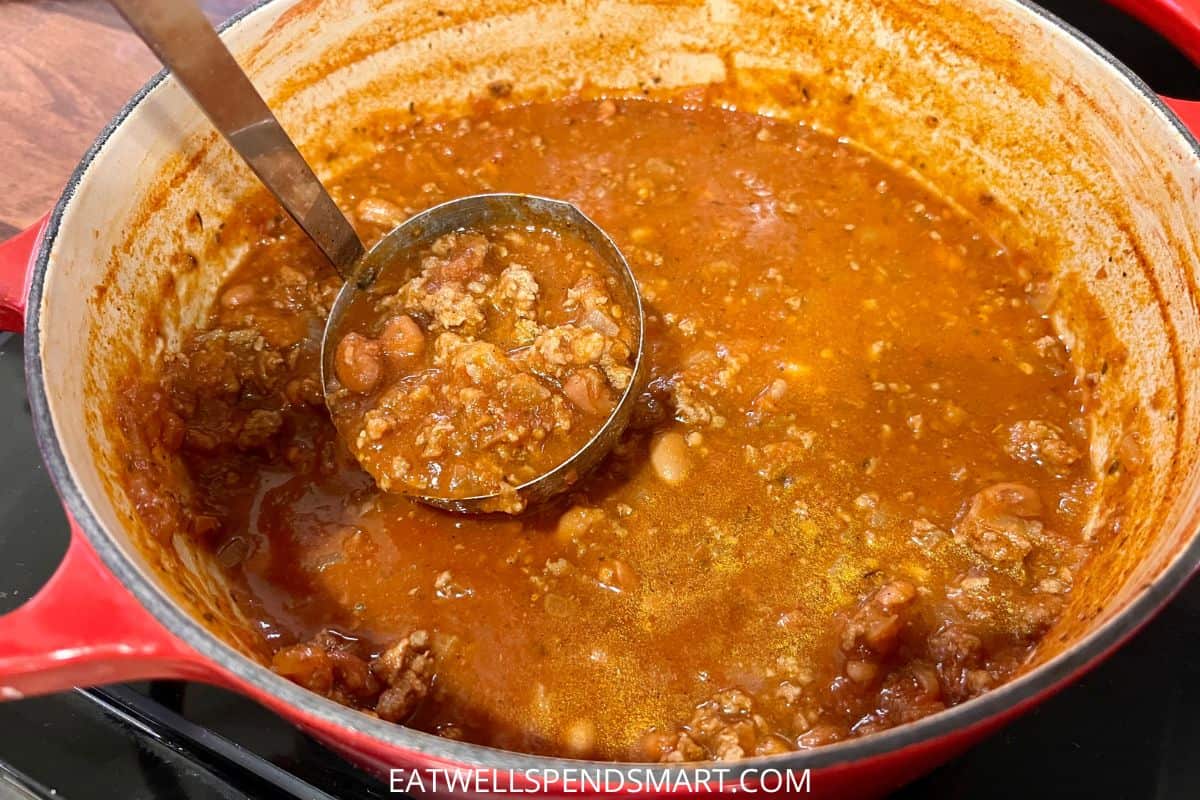 Ladle scooping chili from a red pot