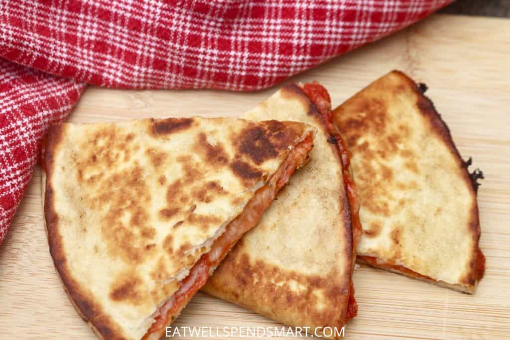 Three pizza quesadilla triangles on a cutting board