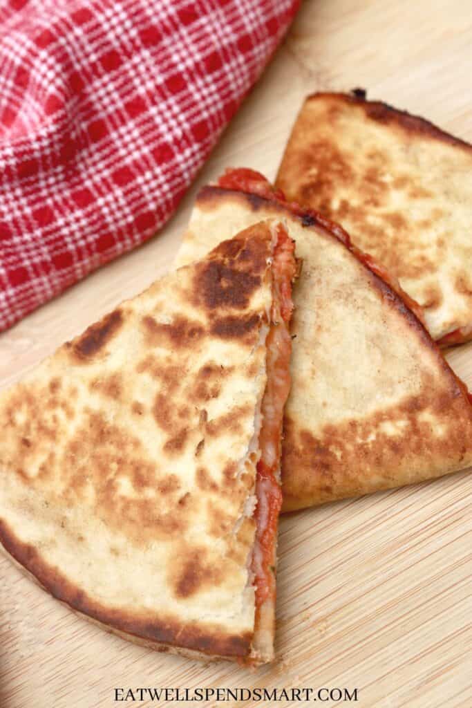 Three wedges of a pizza quesadilla on a cutting board next to a red and white towel.