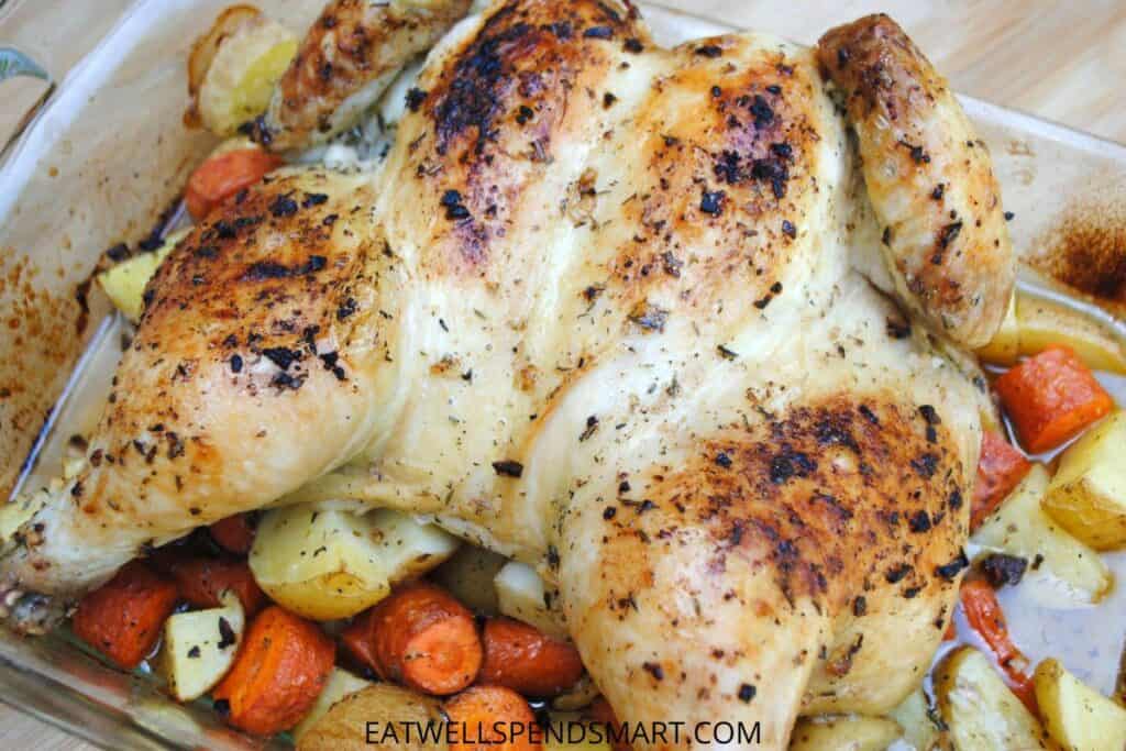 Roasted whole chicken on a bed of roasted potatoes and carrots