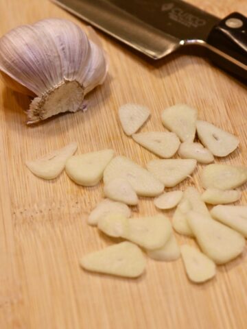 Chef's knife slicing garlic on a cutting board