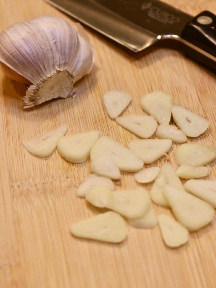 Chef's knife slicing garlic on a cutting board