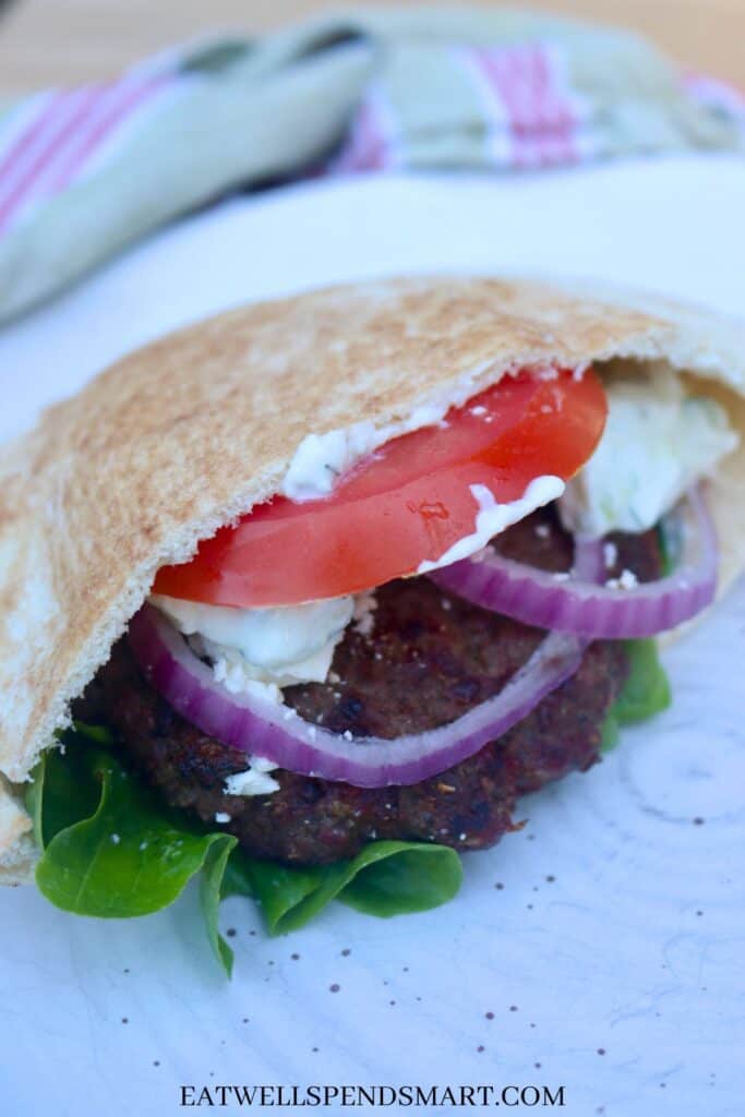 Gyro burger with lettuce, tomato, red onion, and tzatziki on a white plate